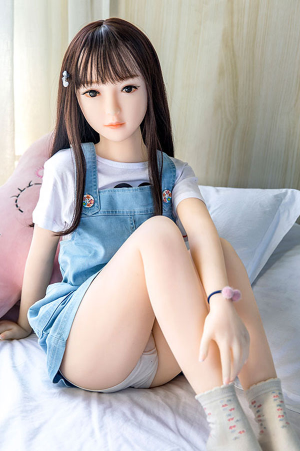 1273 製品ページ:リアルな顔立ちの美少女ラブドール美代、デニムオーバーオール着用、TPE製、ベッドに座る.