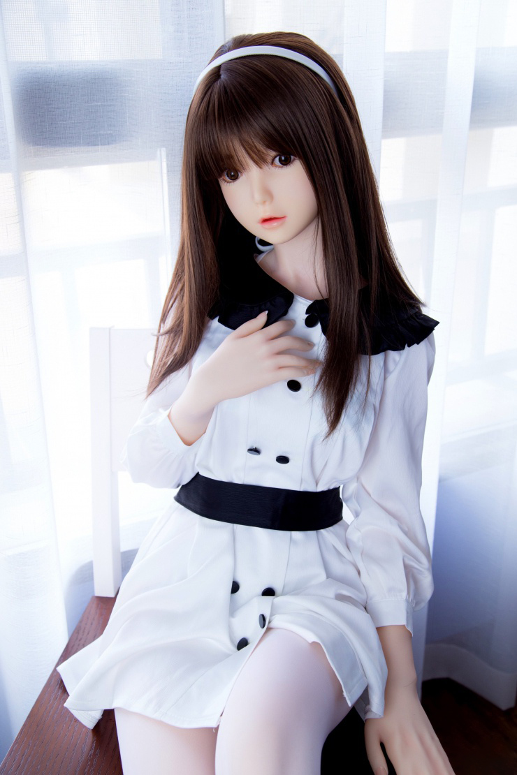 高級 ラブドール ダッチワイフ 美津 138cm 高級ラブドール「美津」138cm、茶髪、白いカチューシャ、白いワンピース、黒いベルト、黒い襟、室内で椅子に座る、リアルな肌の質感を表現.