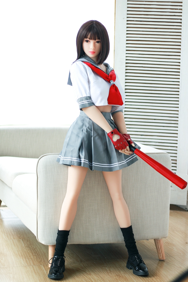 IMG_9302 最新のアイヴァ・コウカ、身長158cm、セーラー服風の衣装、TPE素材。赤いリボンネクタイ、グレーのプリーツスカート、指なし手袋、黒い靴下。ソファの横に立ち、バットを手に持っている。
